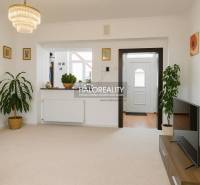 Obývací pokoj v rodinném domě s bílými stěnami, květinami a televizí na stolku.