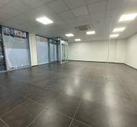 Obchodní prostory s tmavými dlaždicemi, bílými stěnami a skleněnými výlohami.