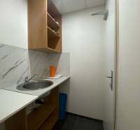 Malá kuchyňka s umyvadlem, policemi a oranžovým džbánem v obchodních prostorách.