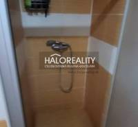 Sprchový kout v 1-pokojovém bytě s oranžovými dlaždicemi a úložným prostorem na stěně.