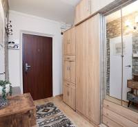 Předsíň 2-pokojového bytu s podlahou s dřevěným dekorem, kamenným obkladem a skříní se zrcadlem.