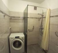 Koupelna se sprchovým koutem, pračkou a světlými obklady ve 3-pokojovém bytě.