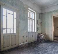 Interiér budovy s poškozenými stěnami, dveřmi a okny, cihly na podlaze.