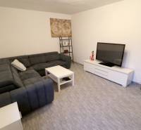 Obývací pokoj v rodinném domě s velkou sedačkou, televizí a malým stolkem.