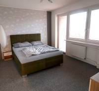 Ložnice v rodinném domě s čalouněnou postelí a šedým kobercem.