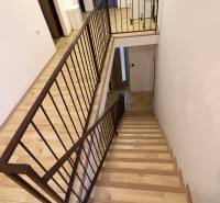 Schodiště v rodinném domě s podlahou s dřevěným dekorem a kovovým zábradlím.