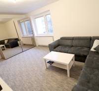 Obývací pokoj v rodinném domě s rohovou sedačkou, zrcadlová skříň, okna, koberec.