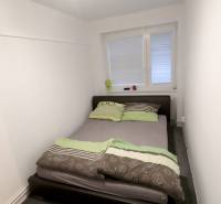 Ložnice s postelí v rodinném domě, bílé stěny, koberec.