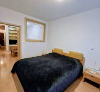 Ložnice se širokou postelí, nočními stolky a podlahou s dřevěným dekorem v dvoupokojovém bytě.