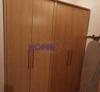 V 2-pokojovém bytě je vidět skříň s dřevěným dekorem a žehlicí prkno.