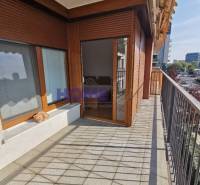 Balkon s dlažbou, dřevěnými okny a výhledem na okolí ve 2-pokojovém bytě.