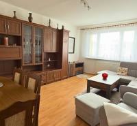 Obývací pokoj v 3-pokojovém bytě s podlahou s dřevěným dekorem a velkou sedací soupravou.