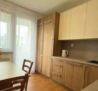 Kuchyně v 3-pokojovém bytě s dřevěným dekorem a světlým nábytkem, elegantní květiny na stole.