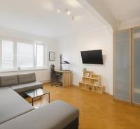 Obývací pokoj ve 3-pokojovém bytě s rohovou sedačkou, pracovním stolem a podlahou s dřevěným dekorem.