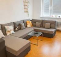 Obývací pokoj s pohodlnou sedačkou a podlahou s dřevěným dekorem v 3-pokojovém bytě.