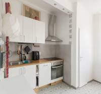 Kuchyně v 3-pokojovém bytě s dlažbou, bílými skříňkami a dřevěným dekorem pultu.