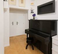 Interiér 3-pokojového bytu se starožitným černým klavírem a podlahou s dřevěným dekorem.