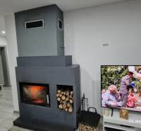 Interiér rodinného domu s krbem a televizí na podlaze s dřevěným dekorem.