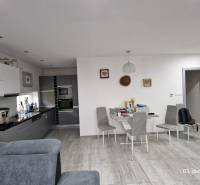 Interiér rodinného domu s kuchyní, jídelním stolem a podlahou s dřevěným dekorem.