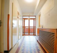 Chodba v rodinném domě s dlažbou a dřevěným krytem na radiátor.