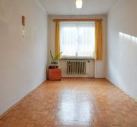 Pokoj v rodinném domě s podlahou s dřevěným dekorem, radiátorem a oknem se záclonou.