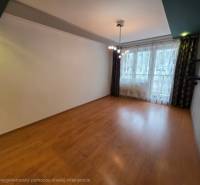 Obývací pokoj čtyřpokojového bytu s podlahou s dřevěným dekorem a velkým oknem.