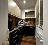 Kuchyně v 1-pokojovém bytě s podlahou s dřevěným dekorem a tmavými skříňkami.