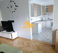 Obývací pokoj v 3-pokojovém bytě s podlahou s dřevěným dekorem a kuchyní v pozadí.