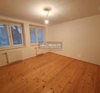 Pokoj rodinného domu s podlahou s dřevěným dekorem, velkými okny a radiátory.