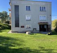 Rodinný dům v Hajnáčce s trávníkem, stromy a zahradním nářadím na dvoře.