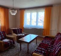 Obývací pokoj v rodinném domě s oranžovými závěsy, sedačkou a konferenčním stolkem.