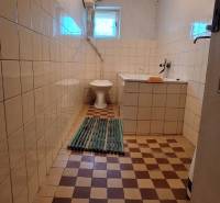 Koupelna v rodinném domě s dlažbou a základním vybavením.