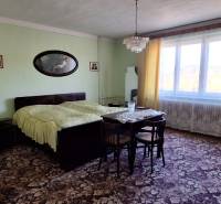 Ložnice v rodinném domě s koberci, postelí a velkým oknem se závěsy.