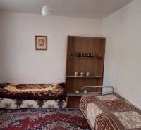 Pokoj v rodinném domě se dvěma postelemi, kobercem a policí na stěně.