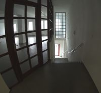 Interiér obchodních prostor s prosklenými dveřmi a schodištěm.