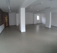 Prostorné obchodní prostory s bílými stěnami a šedou dlažbou, osvětlené stropními světly.