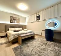 Ložnice ve 4-pokojovém bytě s velkou postelí, koberci a oválným zrcadlem s osvětlením.