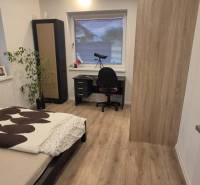 Ložnice s postelí, stolkem a podlahou s dřevěným dekorem v rodinném domě.