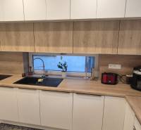 Kuchyně v rodinném domě s bílými skříňkami a pracovní deskou s dřevěným dekorem.