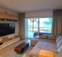 Obývací pokoj rodinného domu s pohovkou, velkou televizí a podlahou s dřevěným dekorem.