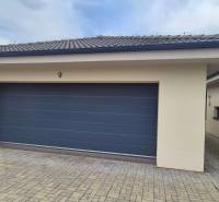 Garáž s dlažbou u rodinného domu ve Studience, s kamennou dlažbou a šedou bránou.