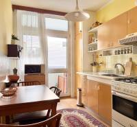 Kuchyňa v 2-izbovom byte s dreveným dekorom podlahy, stolom a kobercom.