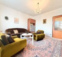 Obývacia izba v 2-izbovom byte so zelenými kreslami, kobercom a lustrom.