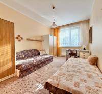 Izba v 2-izbovom byte s gaučom, posteľou, stolom a oknom so závesmi.