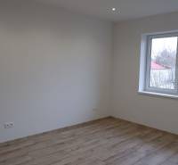 Pokoj v rodinném domě s bílými stěnami a podlahou s dřevěným dekorem.