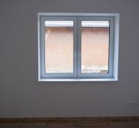 Pokoj v rodinném domě s velkým oknem a podlahou s dřevěným dekorem.