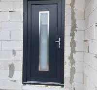 Vstupní dveře rodinného domu v Radavě, obklopené cihlovým zdivem.