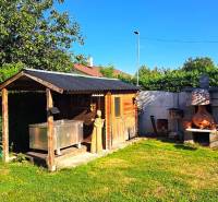 Zahrada rodinného domu v Nedede s dřevěným domkem a venkovním krbem.