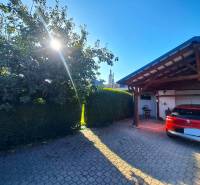 Rodinný dům v Nedede s červeným autem před garáží, slunečný den a strom.