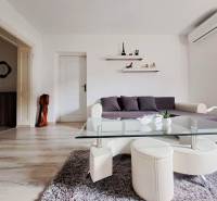 Obývací pokoj v rodinném domě s pohovkou, skleněným stolkem a podlahou s dřevěným dekorem.